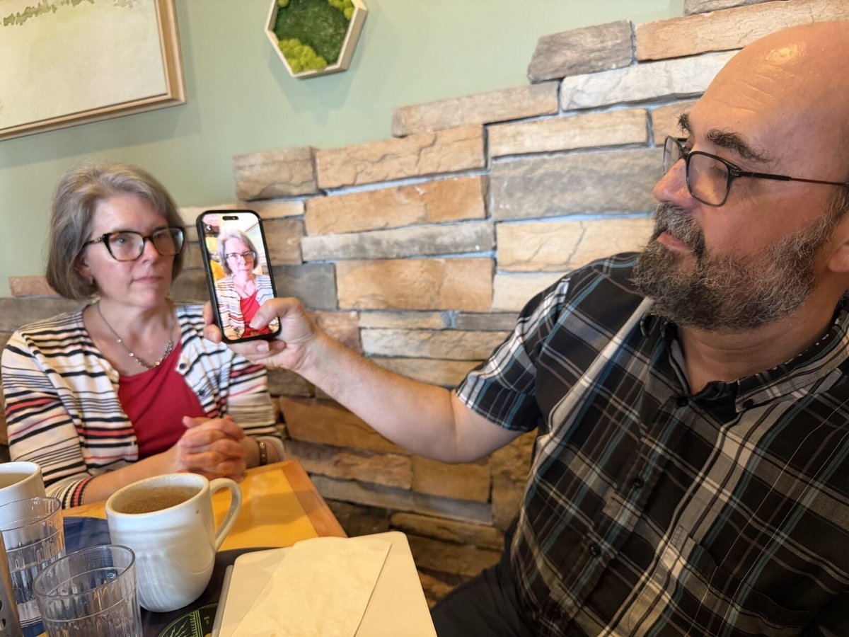 Jeff Heaton holds up his phone, showing the Dynaface app with his wife Tracy's face on screen, across a coffee-shop table from Tracy.